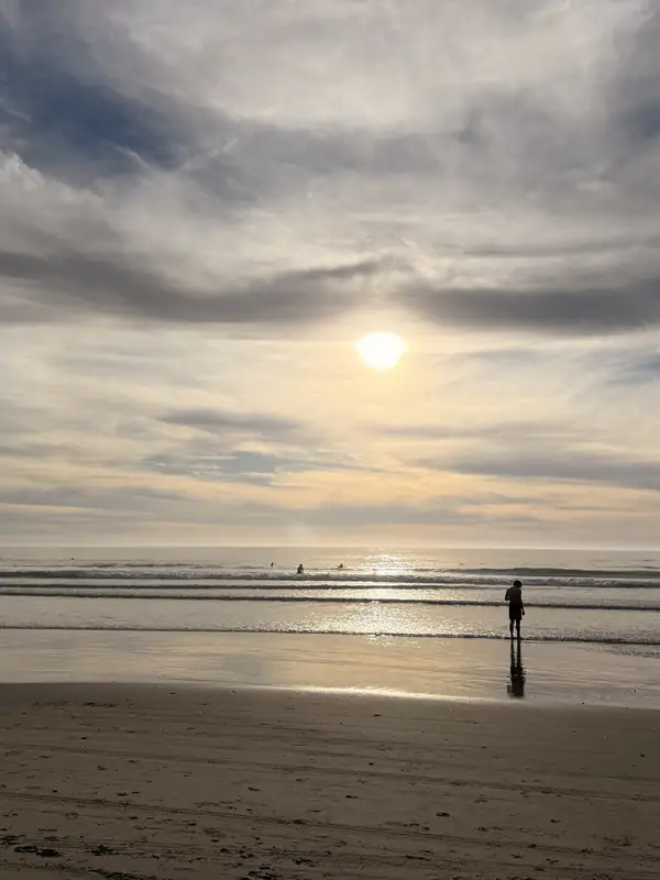 The sun low over the sea below Torrey Pines, with one person on the sand.